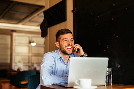 Man with laptop in cafe talking on the phone